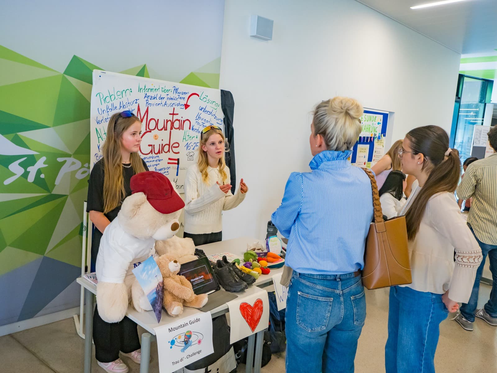 Zwei Schülerinnen stellen Besucherinnen ihr Projekt „Mountain Guide“ an ihrem Stand vor